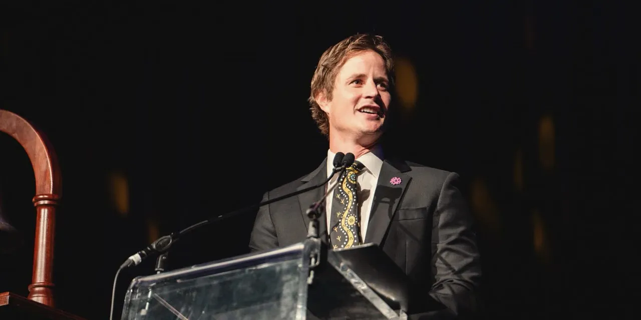 Ross Wallman in a business suit speaking from a lectern at a daytime corporate event